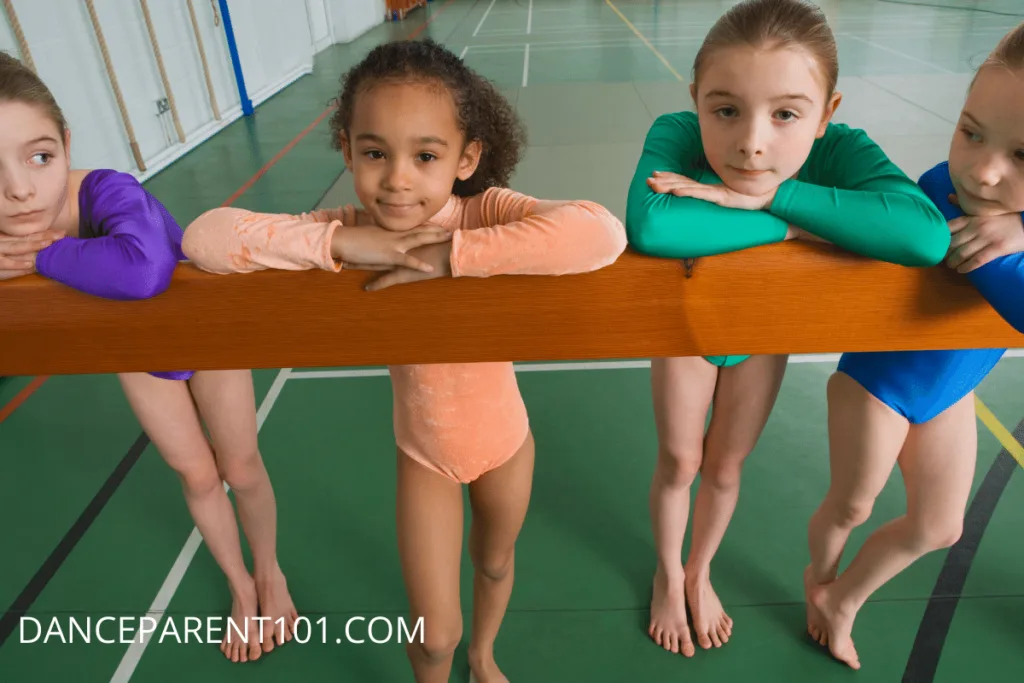 Four Kid Gymnasts standing with the chins on a balance beam