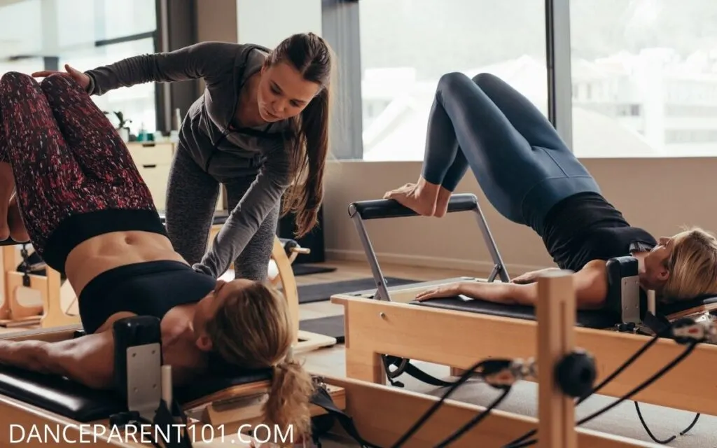 Instructor and two women on pilates Cadillac machines doing a workout