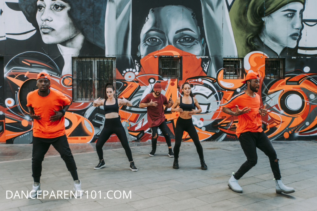 A group of hip hop dancers wearing sneakers dancing in front of a graffiti wall
