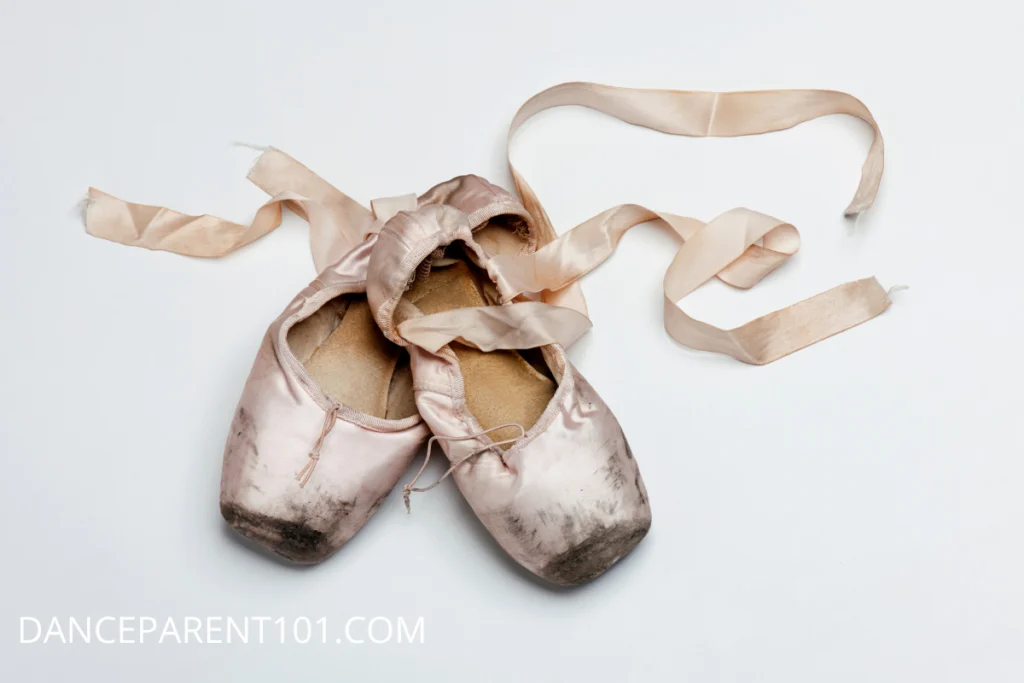 A beat up, old pair of pink pointe shoes on a white background