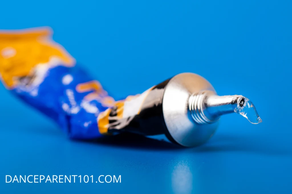 A blue and orange bottle of super glue with a bit of glue coming out sits in front of a blue background