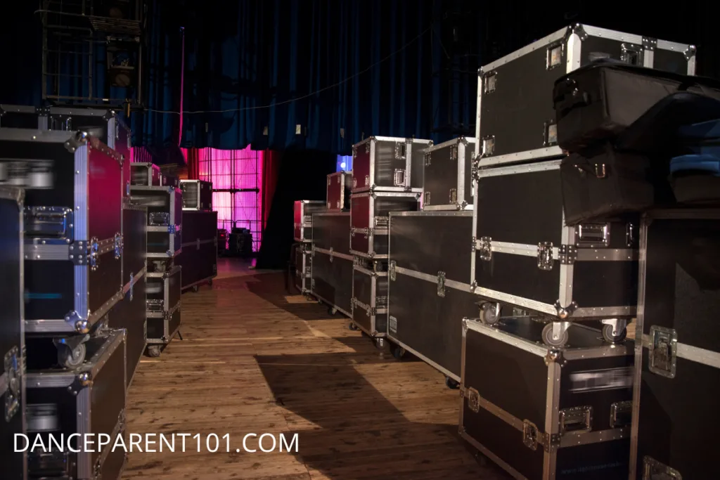 A photo of many black and silver road cases in what looks like the backstage area of a theatre.