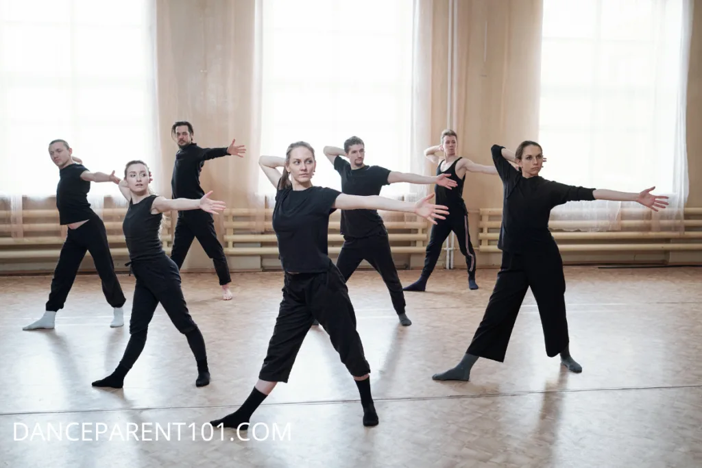 Group of dancers wearing all black clothing and socks in a dance space.