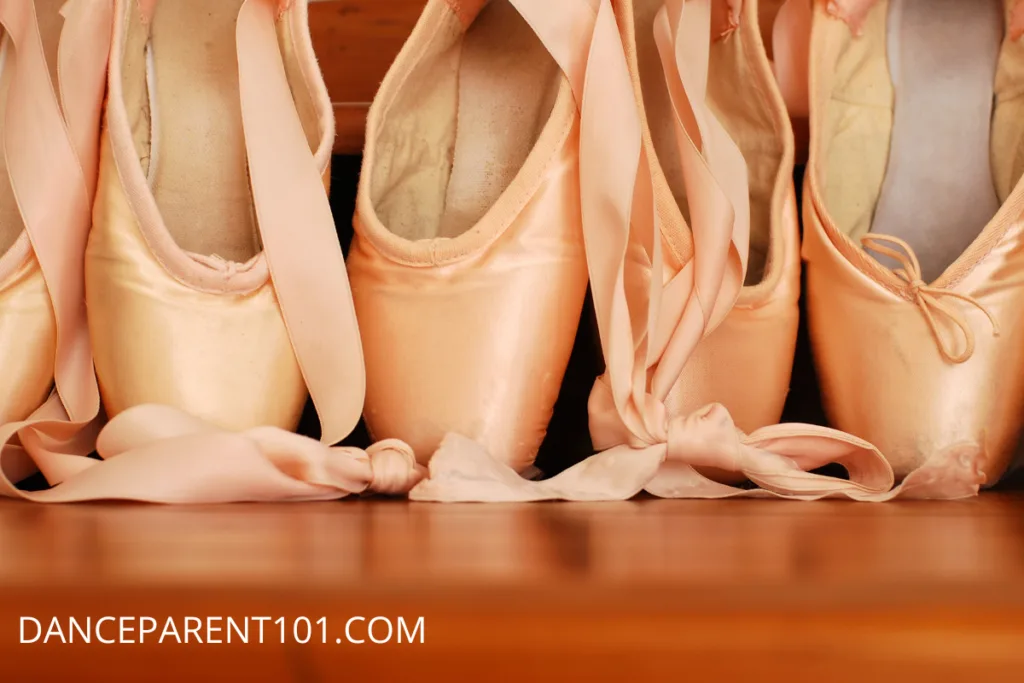 Close up image of 4 pointe shoes, sitting on their boxes on a brown wooden floor